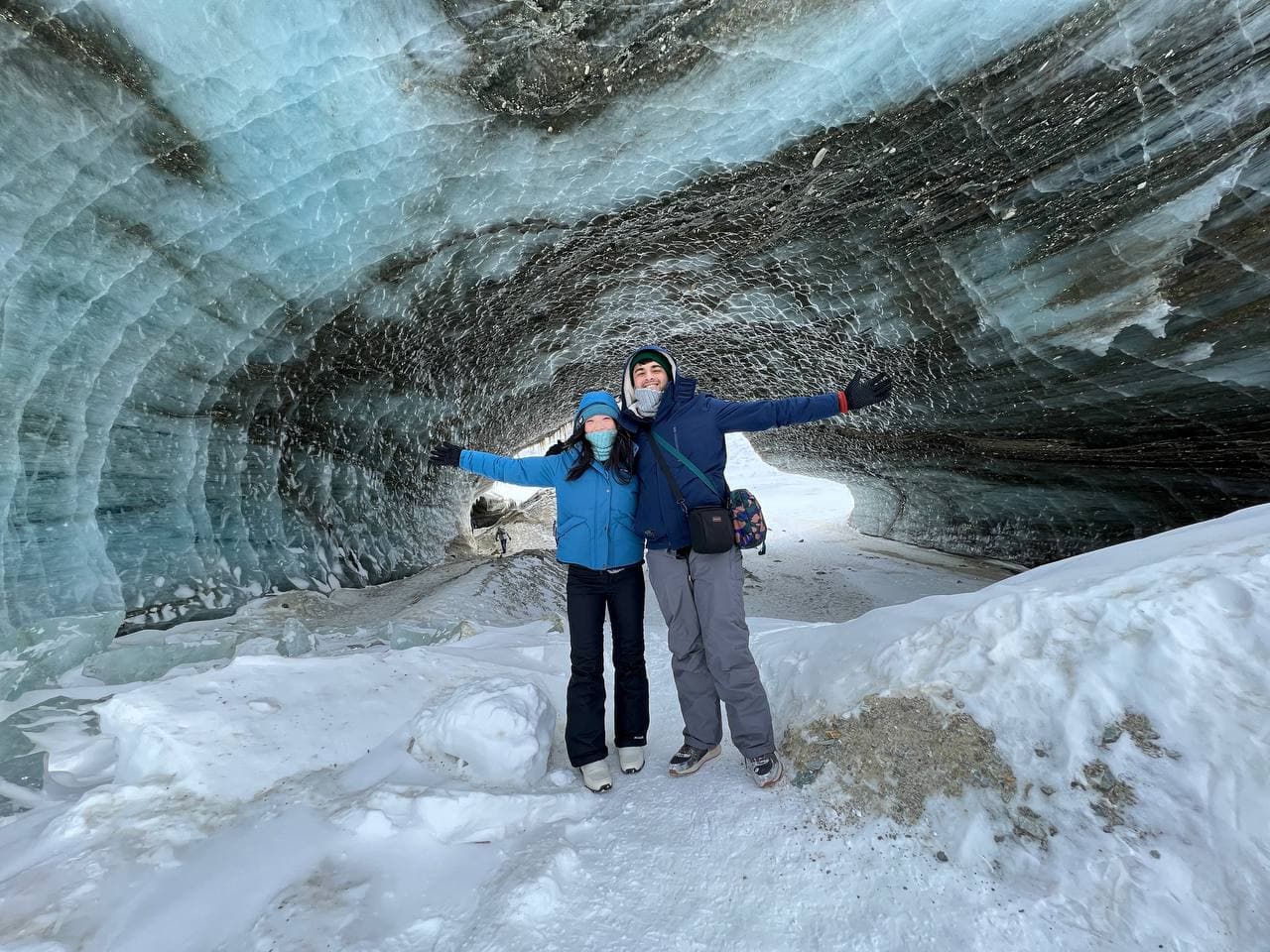 Amy and Roshan with arms outstretched inside a blue ice cave