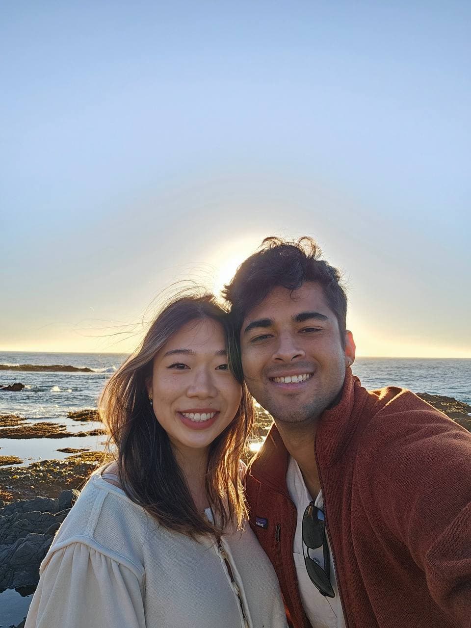 Amy and Roshan smiling together at sunset on the Mendocino coast